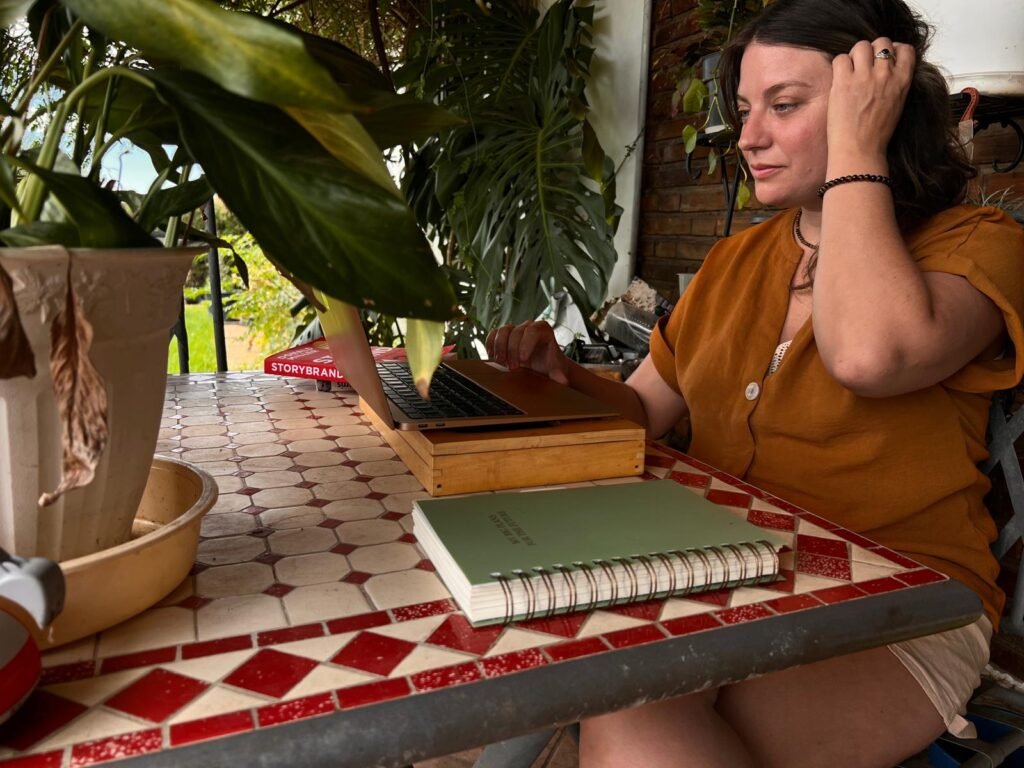 Salud García trabajando en su portátil junto a un cuaderno y el libro StoryBrand, rodeada de plantas